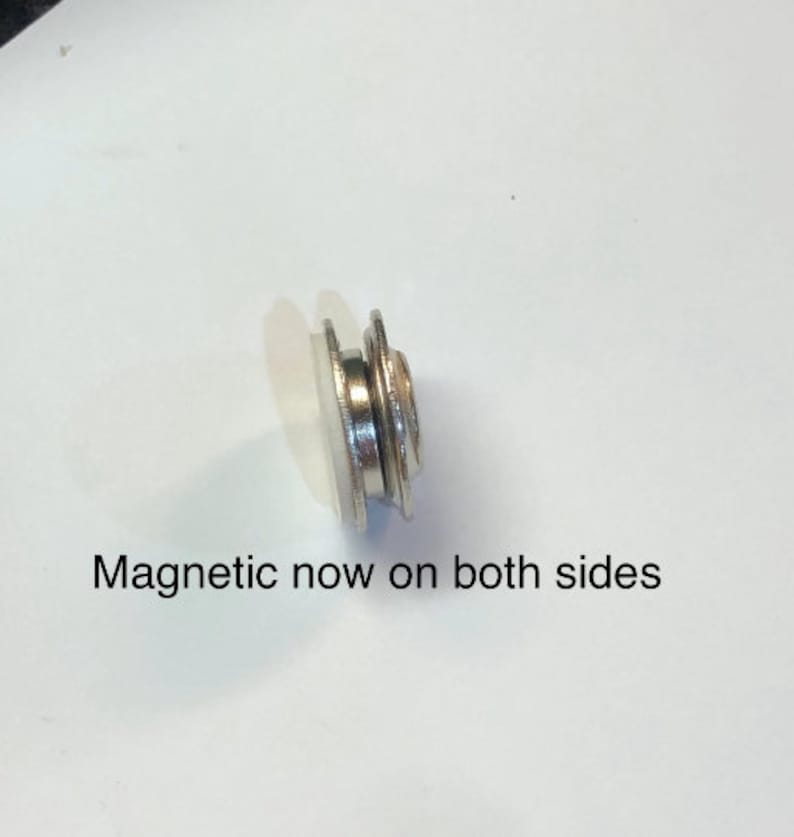 Pode incluir: Um bot&atilde;o magn&eacute;tico prateado com uma base de pl&aacute;stico branco. O texto "Magnetic now on both sides" &eacute; vis&iacute;vel abaixo do bot&atilde;o.