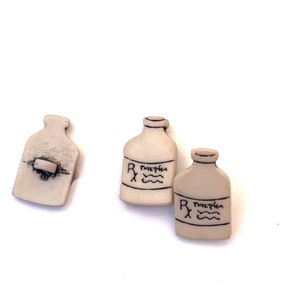 May include: Three off-white, bottle-shaped buttons with black handwritten details. Two buttons have a label with the Rx symbol and the word "Twiefken" above wavy lines. The third button has a button clasp on the back.