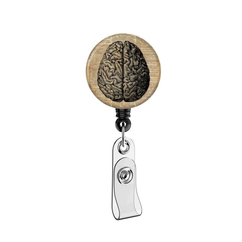 May include: A round, wooden badge reel featuring a detailed illustration of a human brain. The brain image is in black and white, set against a background of aged paper. The reel has a black cord and a silver-colored clip.