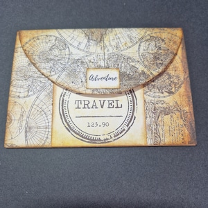 May include: A brown paper envelope with a world map design. The envelope has a flap with a label that says "adventure" and a round stamp that says "TRAVEL" with the number "123.90" underneath.