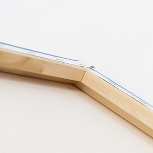 Puede incluir: Primer plano de una esquina de un marco de lienzo de madera. El lienzo est&aacute; tensado sobre el marco y asegurado con grapas. La madera es de color marr&oacute;n claro.