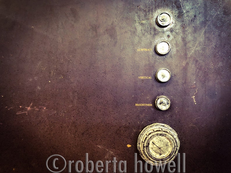 Puede incluir: Primer plano de un panel de control de televisi&oacute;n vintage con cinco botones redondos. Los botones est&aacute;n etiquetados como "Brillo", "Vertical", "Contraste" y dos botones sin etiquetar. El panel es de color marr&oacute;n oscuro con una superficie texturizada.