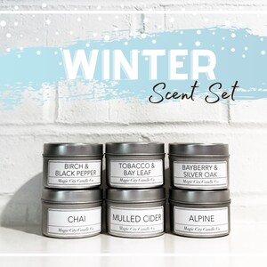 May include: A winter scent set with six small, silver tin candles. Each candle has a white label with the scent name and brand. Scents include Birch & Black Pepper, Tobacco & Bay Leaf, and Chai.
