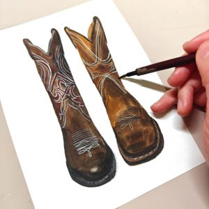 K&ouml;nnte beinhalten: Ein Paar braune Cowboy-Stiefel aus Leder mit wei&szlig;en N&auml;hten und aufwendigen Designs. Die Stiefel sind auf wei&szlig;em Hintergrund gemalt.