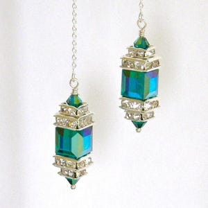 Może przedstawiać: Para kolczyków wiszących ze srebrnym łańcuszkiem i zielonym kryształem w kształcie łzy, ozdobionym przezroczystymi cyrkoniami.