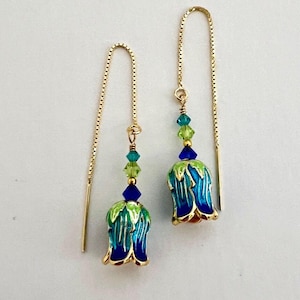 May include: A pair of gold dangle earrings with blue and green enamel flower charms and crystal beads.