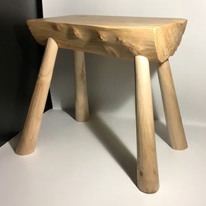May include: A rustic wooden stool with a natural wood finish and four legs. The stool is made from a single piece of wood with a rough, organic texture.
