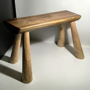 May include: A wooden stool with a natural wood finish and four legs. The stool is made of a single piece of wood and has a rustic look.