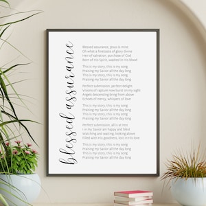May include: A framed print featuring the words "blessed assurance" in a cursive font. The print displays the lyrics to the hymn "Blessed Assurance" in black on a white background. The frame is black.