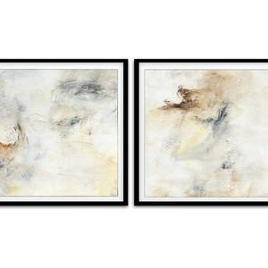 May include: Two abstract paintings in black frames. The paintings are both white with subtle shades of brown, gray, and yellow. The paintings are both abstract and feature brushstrokes and textures.
