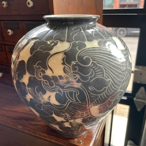 May include: A white ceramic vase with a black and white design of stylized clouds and a dragon. The vase has a round body and a wide mouth.