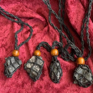 Puede incluir: Cuatro colgantes de cristal negro están encordados en cordones negros con cuentas de madera. Los cristales están encerrados en una red de macramé negro.