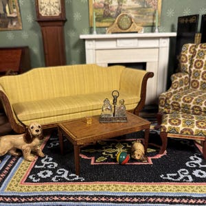 Puede incluir: Escena de sala de estar en miniatura con un sofá amarillo, un sillón estampado y una mesa de centro de madera. Un juego de licor decorativo y un vaso pequeño están sobre la mesa. Una figura de perro y una pelota están en la alfombra.