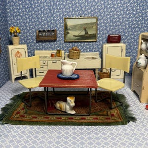 May include: A miniature dining set featuring a red square table with two cream-colored chairs, a white ceramic pitcher on a blue coaster, and a small white and brown dog figurine resting on a green and red patterned rug in a dollhouse kitchen.
