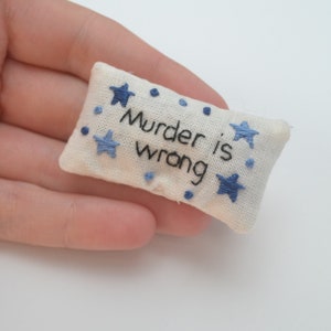 May include: A small white cushion with blue embroidered stars and the text "Murder is wrong".