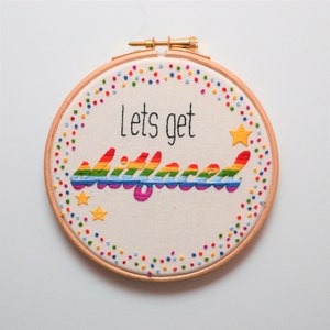 May include: Embroidered hoop art featuring a rainbow design and the text "Lets get lit, fam". The hoop is surrounded by a border of colourful dots.