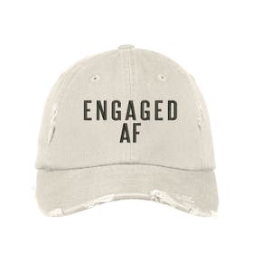 May include: A light beige distressed baseball cap with black embroidered text that reads "ENGAGED AF".