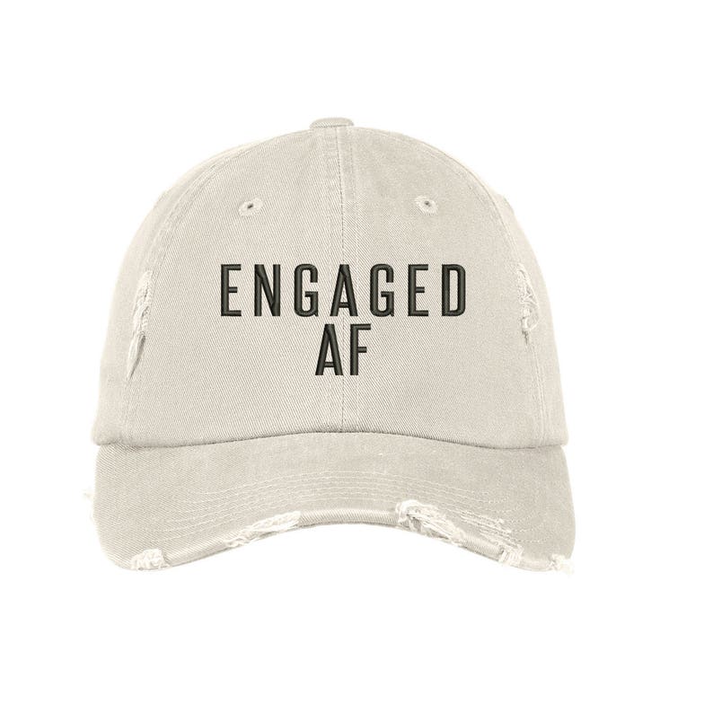 May include: A light beige distressed baseball cap with black embroidered text that reads "ENGAGED AF".