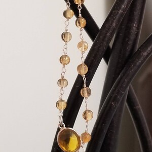 K&ouml;nnte beinhalten: Ein gold- und silberfarbenes Armband mit einem gro&szlig;en, ovalen, gelben Edelstein. Das Armband besteht aus kleinen, runden, goldenen Perlen und silbernen Kettengliedern.