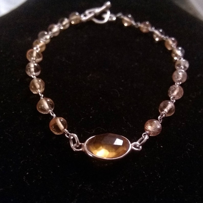 K&ouml;nnte beinhalten: Ein silbernes Armband mit einem gro&szlig;en ovalen Topas-Edelstein und kleineren runden Topas-Perlen.