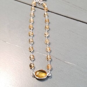 K&ouml;nnte beinhalten: Ein silbernes Kettenarmband mit einem gro&szlig;en ovalen Citrin-Edelstein. Die Kette besteht aus kleinen, runden Perlen.