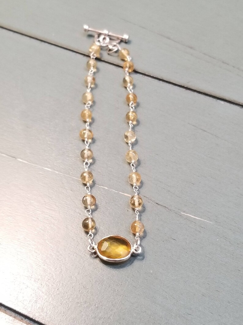 K&ouml;nnte beinhalten: Ein silbernes Kettenarmband mit einem gro&szlig;en ovalen Citrin-Edelstein. Die Kette besteht aus kleinen, runden Perlen.
