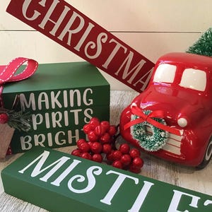 May include: A festive Christmas display featuring a red truck carrying a green tree, a green box with a red ribbon, and a red sign that says "CHRISTMAS". The box says "MAKING SPIRITS BRIGHT".