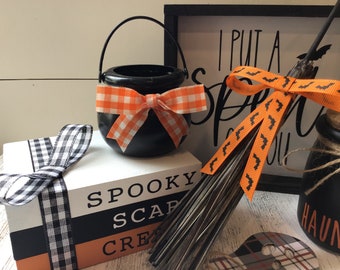May include: Halloween decorations with a black cauldron with an orange and white checkered ribbon, a black and white checkered ribbon, a broom with an orange ribbon with black bats, a black and white sign that says "I put a spell on you", and a black jar with the word "Haunted" on it.