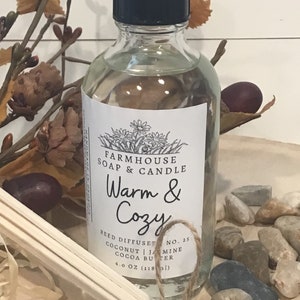 May include: A clear glass bottle with a black lid and a white label. The label says "Farmhouse Soap & Candle Warm & Cozy Reed Diffuser No. 25 Coconut | Jasmine Cocoa Butter 4.0 oz (118 ml)".