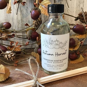 May include: A clear glass bottle with a black lid and a white label. The label reads "Autumn Harvest Farmhouse Soap & Candle Reed Diffuser" and lists the scents "Ripe Fig | Black Plum | Balsam Fir | Cedar". The bottle is 4.0 oz (118 ml).