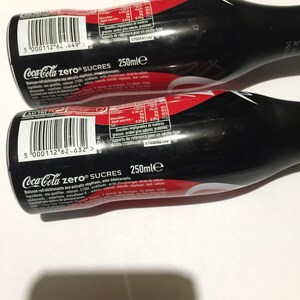 May include: Two black Coca-Cola Zero Sugar bottles with nutritional information printed on the labels. The bottles are 250 ml each.