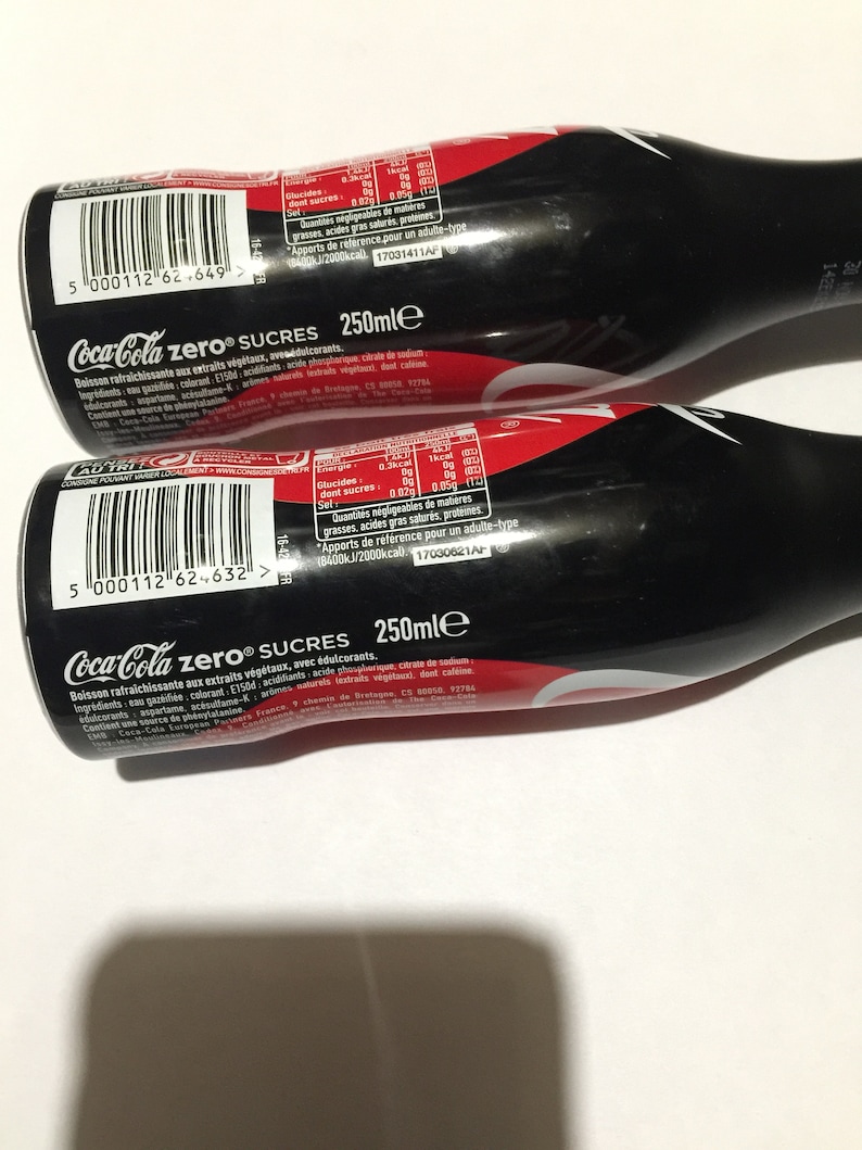 May include: Two black Coca-Cola Zero Sugar bottles with nutritional information printed on the labels. The bottles are 250 ml each.