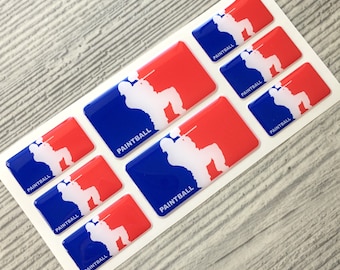 May include: A sheet of glossy stickers featuring a paintball player silhouette in white, set against a red and blue background. The word "PAINTBALL" is printed in white. The stickers are rectangular and have a rounded edge.