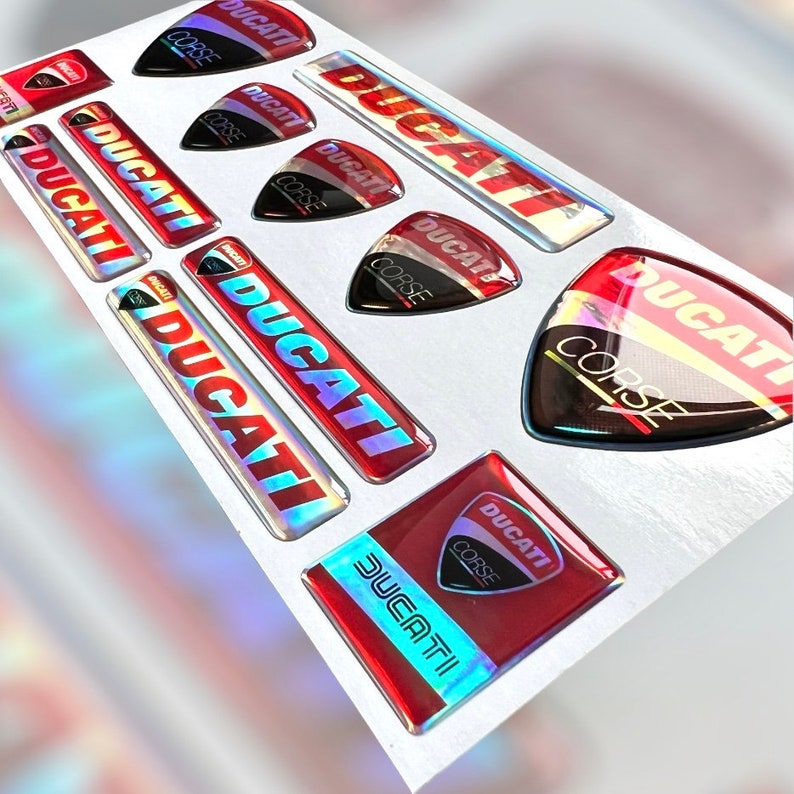 Op de afbeelding: Een set van 10 rode en witte Ducati Corse stickers met een holografische afwerking. De stickers bevatten het Ducati Corse logo en de woorden "Ducati Corse".