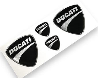 Op de afbeelding: Vier zwarte en zilveren 3D-stickers met het woord "DUCATI" in witte letters.