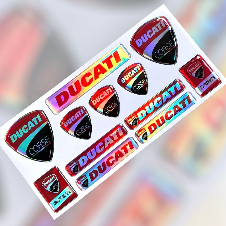Op de afbeelding: Een vel met rode, zwarte en zilveren holografische stickers met de tekst "DUCATI" en "CORSE" erop gedrukt.