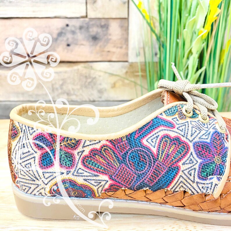 Pu&ograve; includere: Primo piano di una scarpa beige e marrone con un motivo floreale colorato. La scarpa ha una suola in pelle intrecciata e una chiusura con lacci.