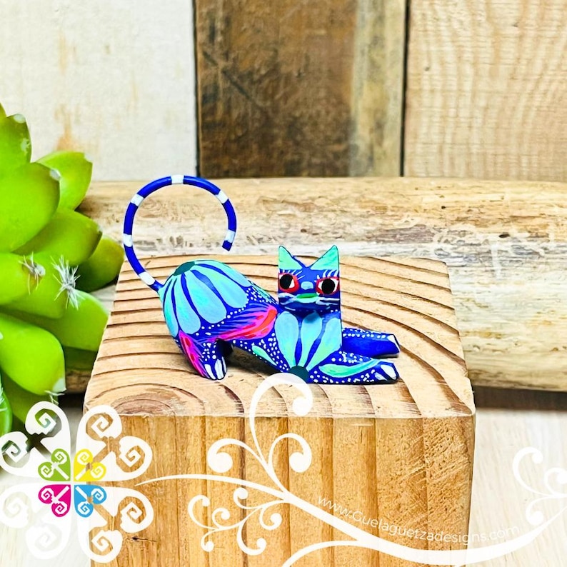 May include: A blue and white hand-painted wooden cat figurine with a floral design. The cat is lying down with its tail curled up.