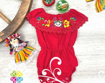 May include: Red embroidered baby onesie with a floral design and a small embroidered figure. The onesie has a ruffled neckline and a white lace trim.