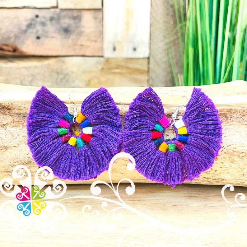 May include: A pair of vibrant purple tassel earrings. Each earring features a fan-shaped design with a colorful beaded center. The earrings are suspended from silver-colored hooks, offering a bold and artistic statement.