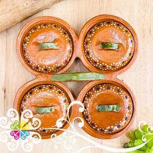 May include: Four terracotta serving dishes with lids, each with a green garnish. The dishes are arranged in a cloverleaf pattern and decorated with white polka dots. The overall design is rustic and handmade.