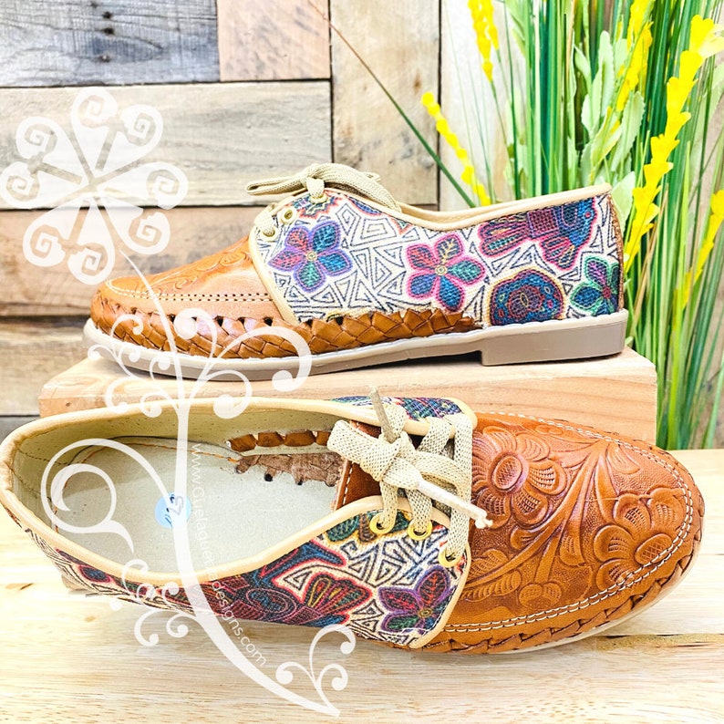 Pu&ograve; includere: Un paio di scarpe in pelle marrone con pannelli in tessuto ricamato colorato e dettagli in pelle intrecciata. Le scarpe hanno lacci e una punta arrotondata.
