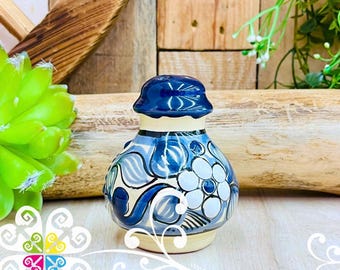 Pode incluir: Um saleiro de cerâmica pintado à mão com um design floral azul. O saleiro tem uma tampa azul escura e uma base creme. O corpo do saleiro é decorado com padrões florais e redemoinhos azuis e brancos.