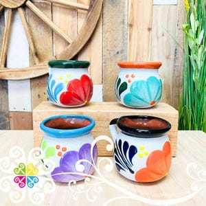 May include: Four small, white ceramic mugs with colorful floral designs. Each mug has a different floral pattern with red, blue, orange, and purple flowers. The mugs are hand-painted and have a rustic, handmade look.