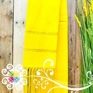 May include: A bright yellow rectangular textile featuring two horizontal bands of intricate openwork embroidery and a fringe of long, thin yellow threads at the bottom edge. The fabric has a smooth, solid color finish throughout the main body.