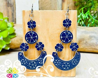 May include: A pair of blue and white ceramic earrings with a floral design. The earrings are made of three layers of ceramic, each with a different floral pattern. The earrings are suspended from silver hooks.