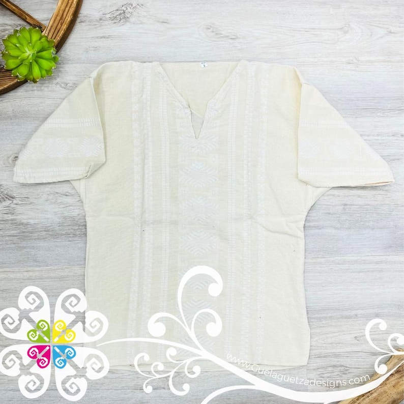 May include: A white cotton embroidered tunic with a V-neckline. The embroidery is a geometric pattern in white thread.