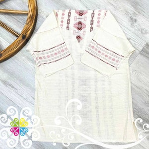 May include: A white linen tunic with pink and red embroidered details on the neckline and sleeves. The tunic has a V-neck and short sleeves.