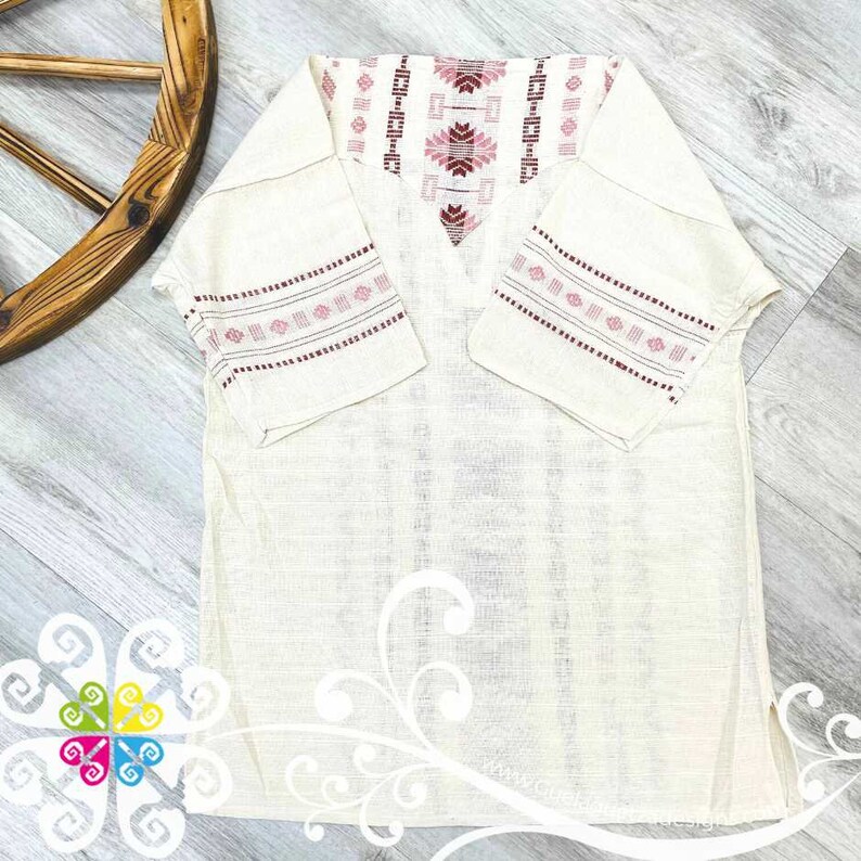 May include: A white linen tunic with pink and red embroidered details on the neckline and sleeves. The tunic has a V-neck and short sleeves.