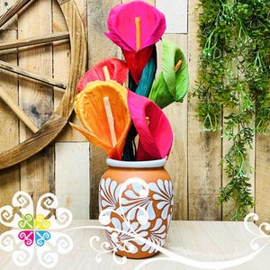 May include: A bouquet of colorful paper flowers in a white and brown ceramic vase with a floral design. The flowers are made of paper and are in shades of pink, orange, and yellow.